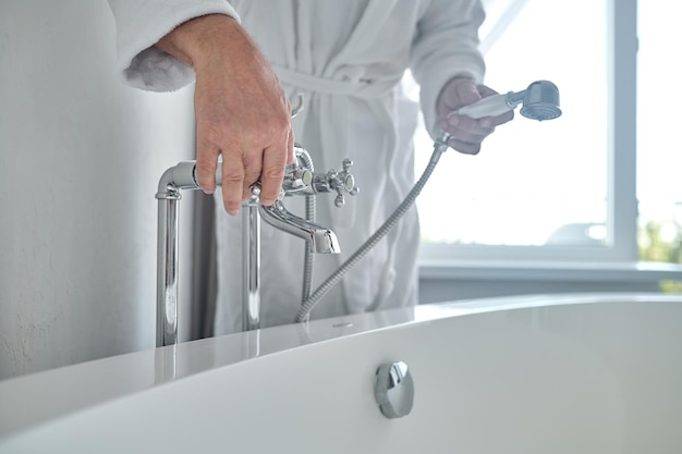 욕조에 물을 채우는 흰색 테리 목욕 가운을 입은 남자