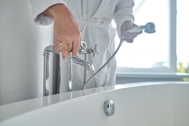 白いテリーの風呂衣を着た男が浴槽を水で満たしている