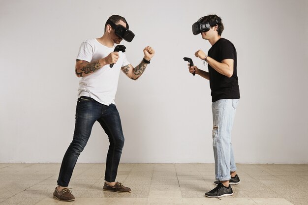 A man in white unlabeled t-shirt with bear and tattoos and a man in black unlabeled t-shirt wearing VR headsets fight in a room with white walls.