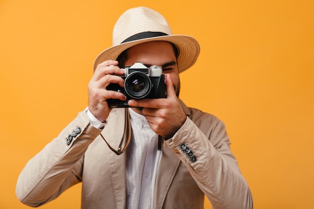 つばの広い帽子をかぶった男がレトロなカメラで写真を撮る