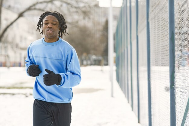 Man in a winter park. African guy training outside. Man run.