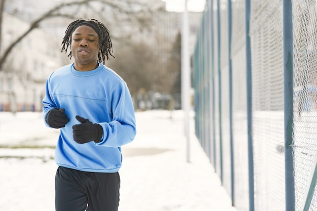 Человек в зимнем парке. Африканский парень тренируется на улице. Человек, беги.