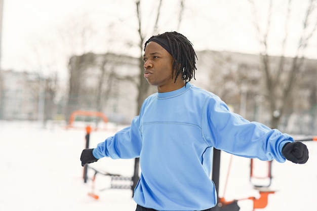 Man in a winter park. African guy training outside.