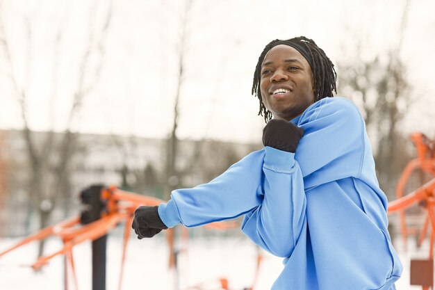 Man in a winter park. African guy training outside.