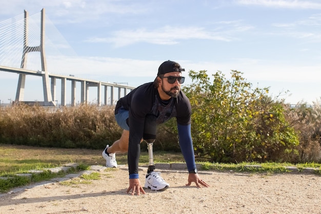 Man with artificial leg at track. Man in sport clothes stretching in park on summer day, exercising. Sport, training, disability concept