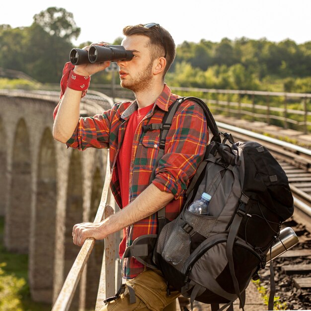 Man with backpack at bridge looking with binocular