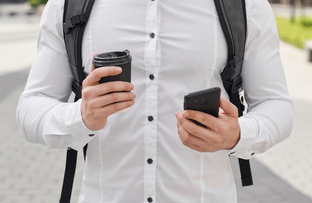 Man with backpack holding black phone and coffee cup