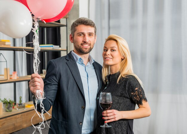 Человек с воздушными шарами возле женщины с бокалом вина в комнате