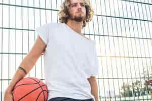 Free photo man with basketball standing in front of fence