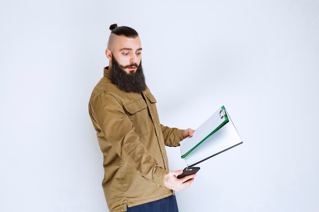 Man with beard checking the accounting reports and calculating at telephone.