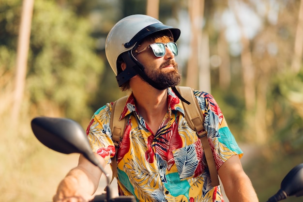 Man with beard in colorful tropical shirt sitting on motorbike