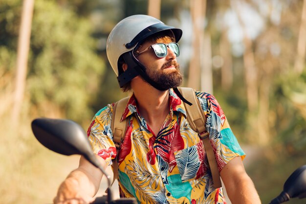 Человек с бородой в красочной тропической рубашке сидит на мотоцикле