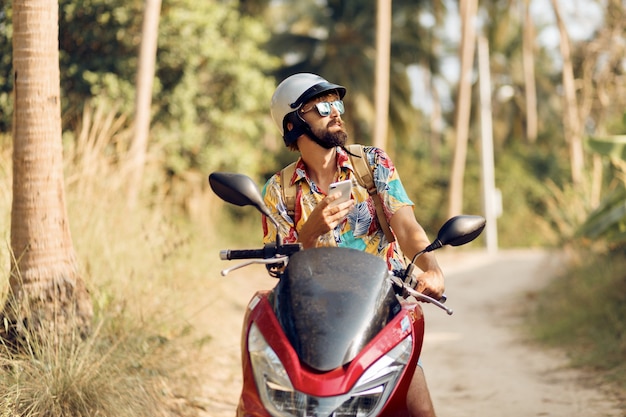 Man with beard in colorful tropical shirt sitting on motorbike