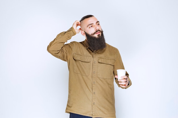 Man with beard holding a cup of coffee and thinking.