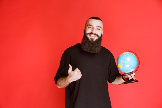 Man with beard holding a globe and pointing to somewhere.