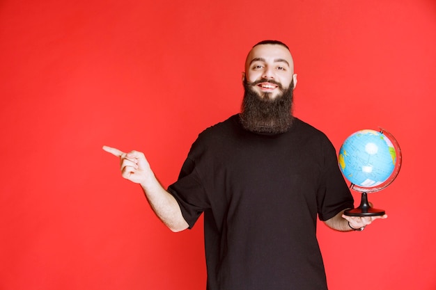 Man with beard holding a globe and pointing to somewhere.