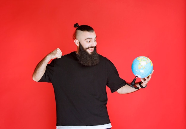 Uomo con la barba che tiene un globo e mostra il pugno.