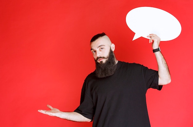 Man with beard holding an ovale thinkboard and pointing at somebody.