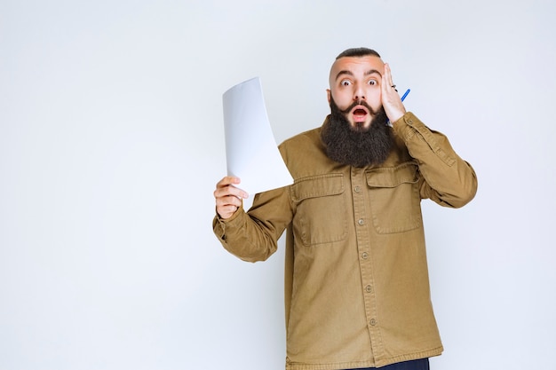 Man with beard holding a quiz paper and looks confused and thoughtful. 