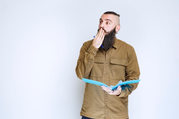 Man with beard holding a quiz paper and looks confused and thoughtful.  