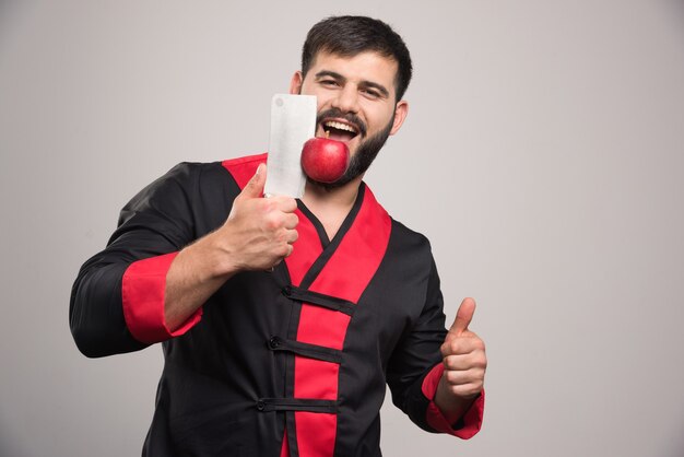 Man with beard holding red apple on knife .