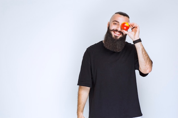 Man with beard holding a red apple or peach. 