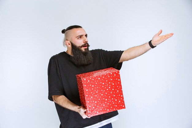 Мужчина с бородой держит красную подарочную коробку и спорит с кем-то.