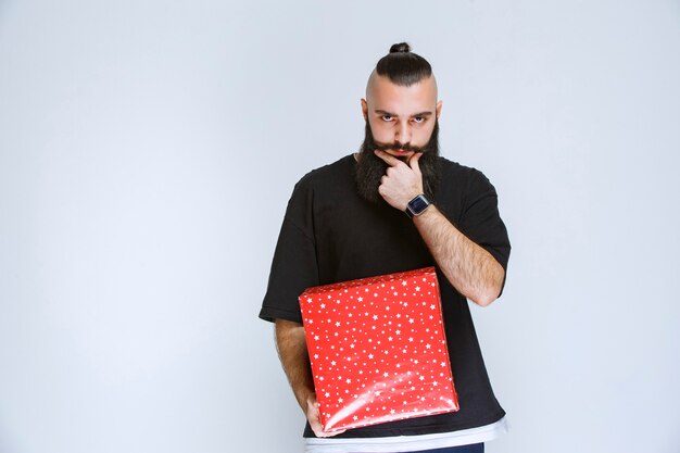 Free photo man with beard holding red gift boxes and hesitating about making choise.