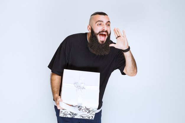 Man with beard holding a white blue gift box smiling and feeling happy. 