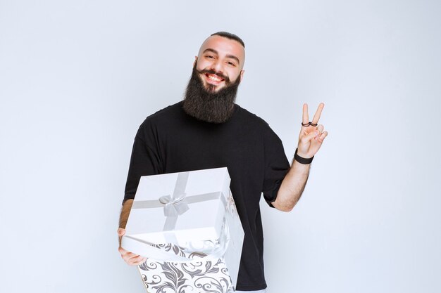 Man with beard holding a white blue gift box smiling and feeling happy. 