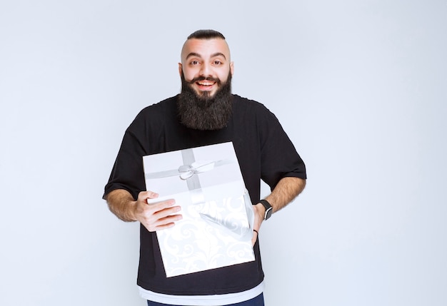 Man with beard holding a white blue gift box smiling and feeling happy. 