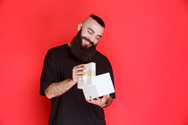 Man with beard holding a white gift box and opening it with excitement.