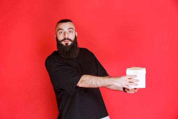 Man with beard holding a white gift box with satisfaction.