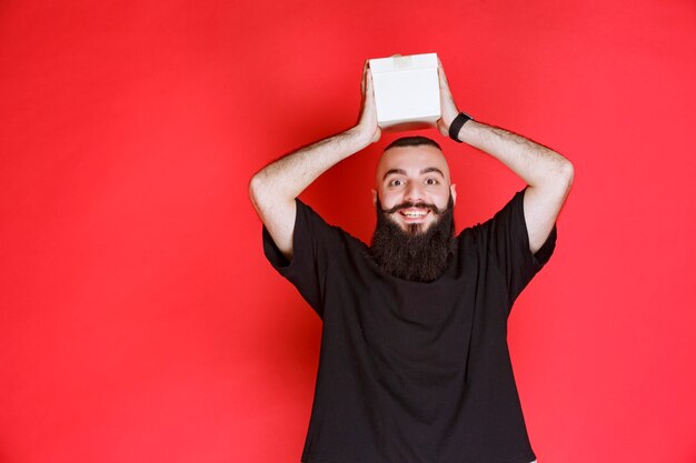 Man with beard holding a white gift box with satisfaction.