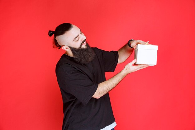 Man with beard holding a white gift box with satisfaction.