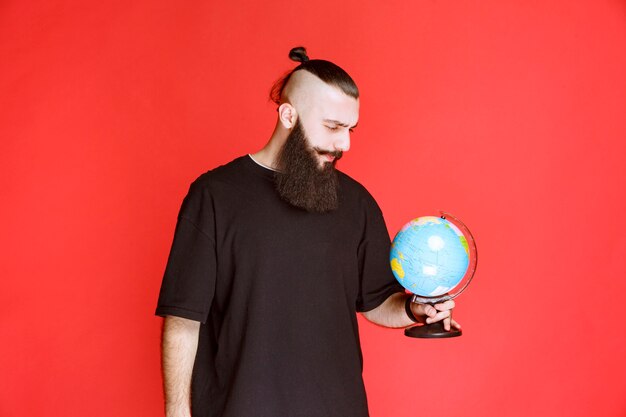 Man with beard holding a world globe and looking for places over it.