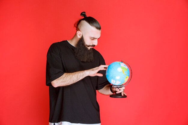 ひげを生やした男が世界の地球儀を持って、その上の場所を探しています。