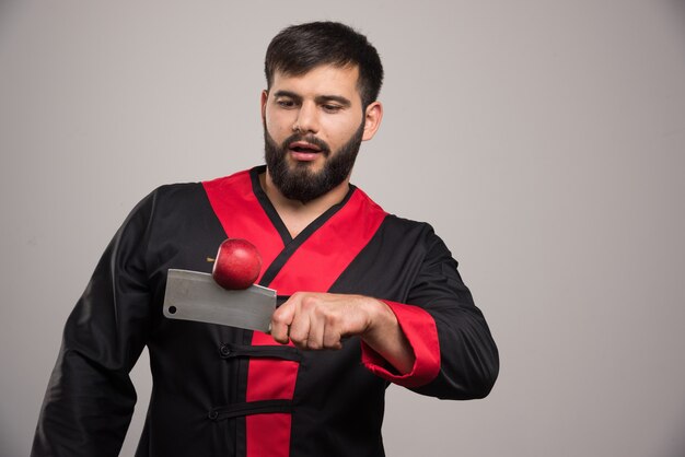 Man with beard looking on red apple on knife .