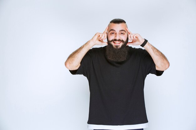 Man with beard poining his head, smiling and thinking. 