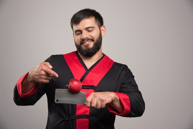 Man with beard pointing at red apple on knife .