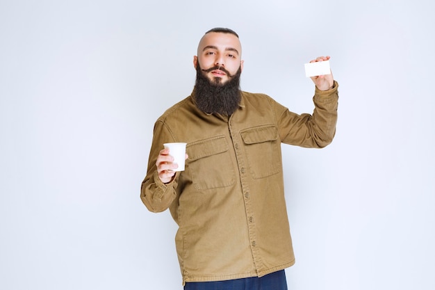 Man with beard showing his business card while holding a cup of coffee.