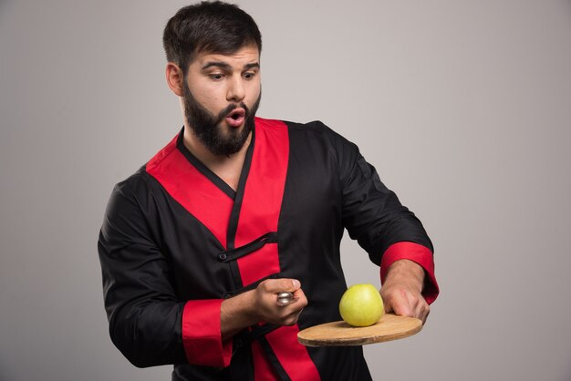 Man with beard trying to cut an apple on wooden board .