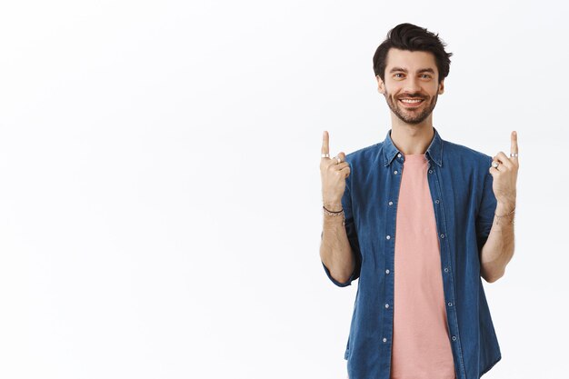 man with beard, wearing pink t-shirt, shirt, pointing up and looking camera, showing gifts he bought, invite people visit link, recommend cool party