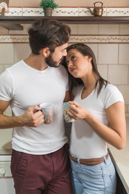 Man with beverage looking at girlfriend in kitchen