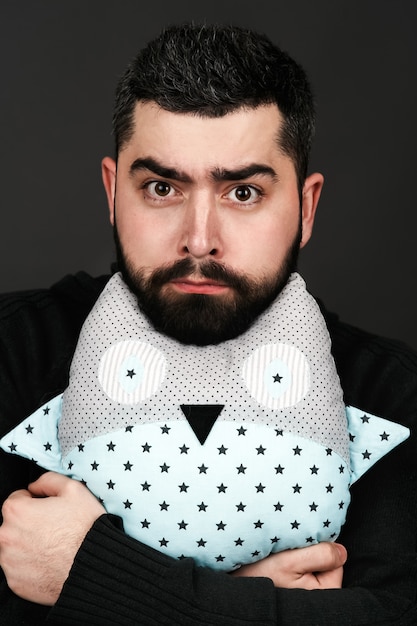 Man with black beard holds toy pillow in form of an owl