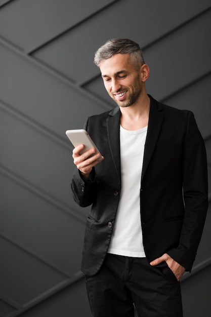 Человек с черным пиджаком улыбается на своем мобильном телефоне