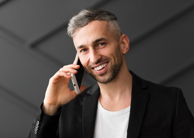 Man with black jacket talks on the phone and smiles