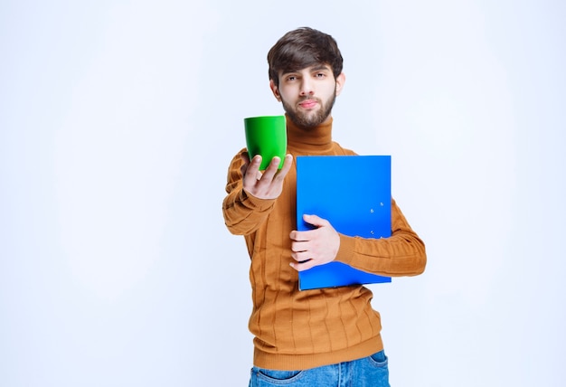 Man with a blue folder offering a green cup of drink.