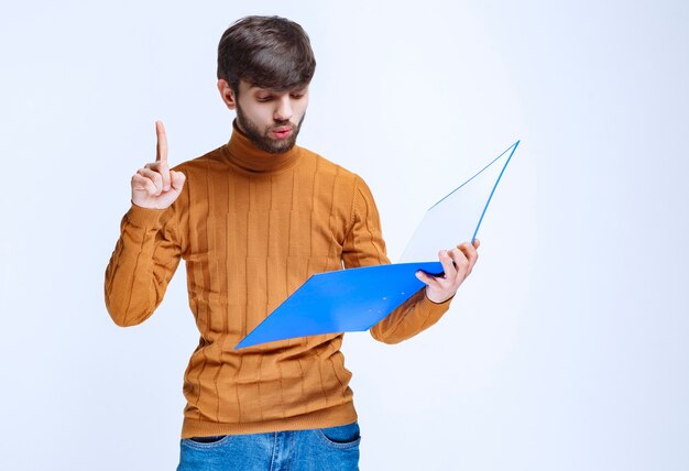 Man with a blue folder raising finger for attention.