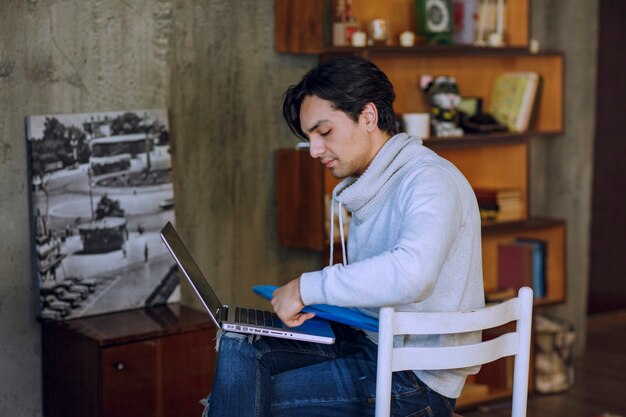 Человек с голубой папкой работает на ноутбуке и выглядит усталым. Фото высокого качества